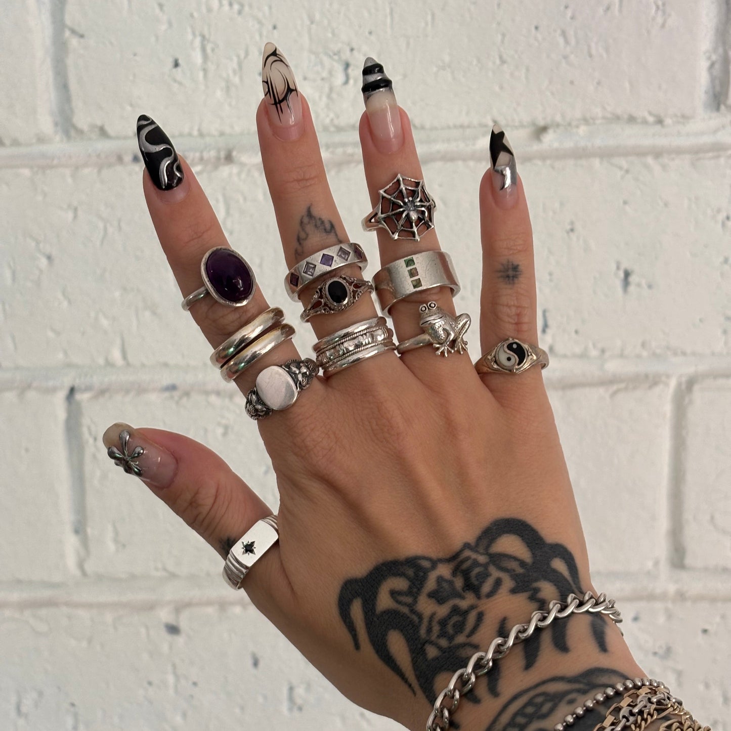 Hand with multiple rings and bracelets against a white brick wall background